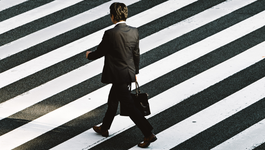 An image of a business man in a black suit walking in a crosswalk