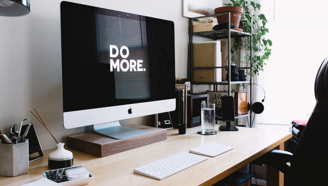 A modern home desk with a large computer screen that reads 'Do More'