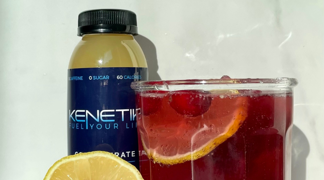 The Kenetik Concentrate bottle next to a refreshing cranberry ketone drink and lemon