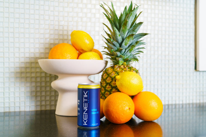 Kenetik RTD in a can on a kitchen counter with pineapple, oranges and lemons in the background